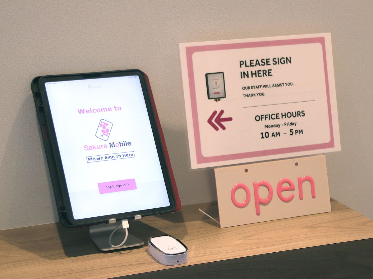Tablet showing 'Welcome to Sakura Mobile' and office hours at Shinjuku pickp location.