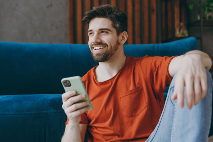 A man is casually sitting in a chair smiling while holding his phone